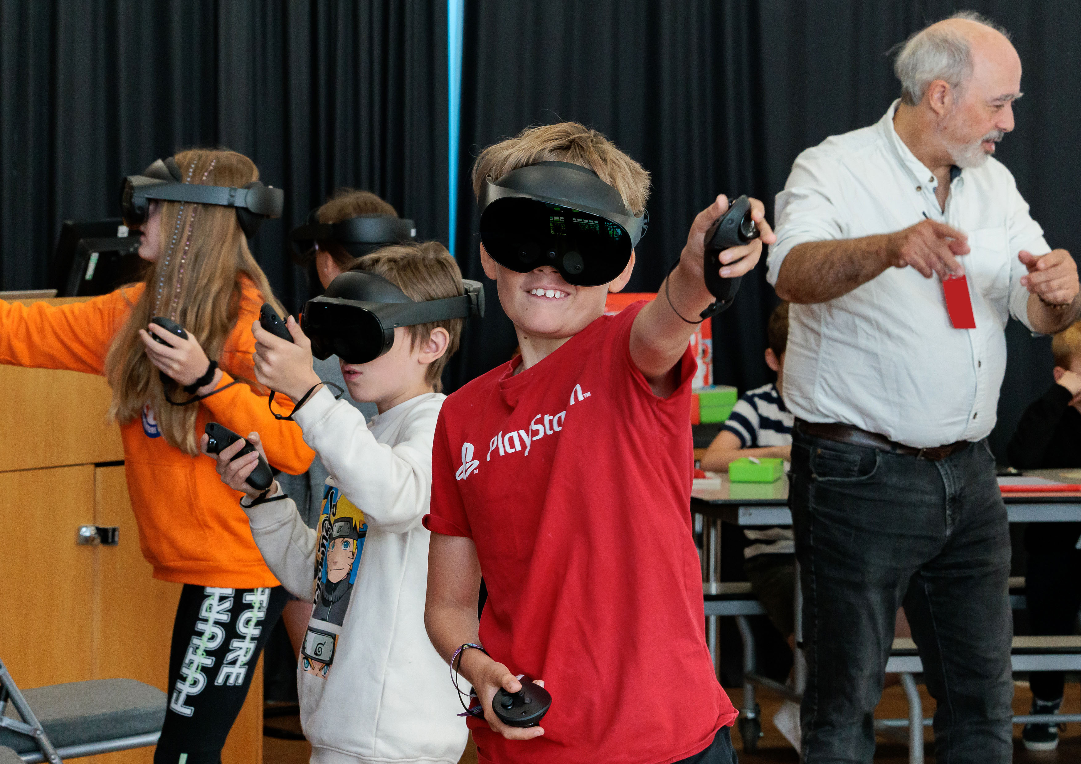 Photo: A group of 'Summer of STEM' students are standing, whilst engaged in a STEM activity, wearing Virtual Reality headsets and holding controllers.